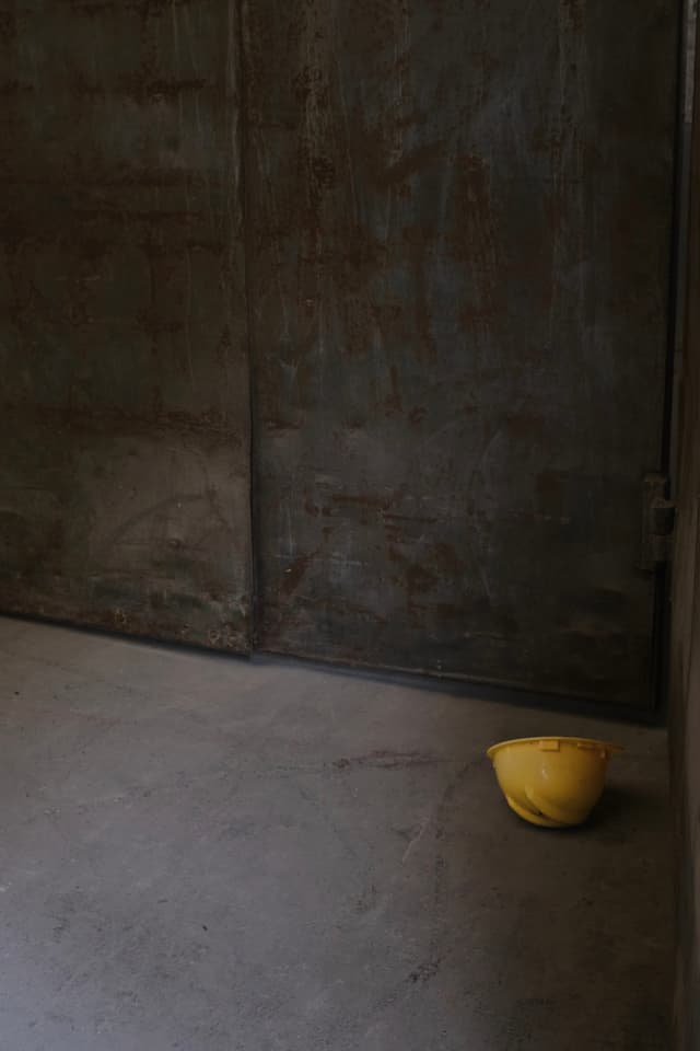 A yellow hard hat rests on the floor in a room with weathered metal walls